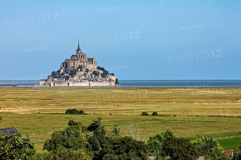 Historic abbey on a rocky island off the coast of France, surrounded by green fields and blue skies, Mont Saint Michel in Normandy, France