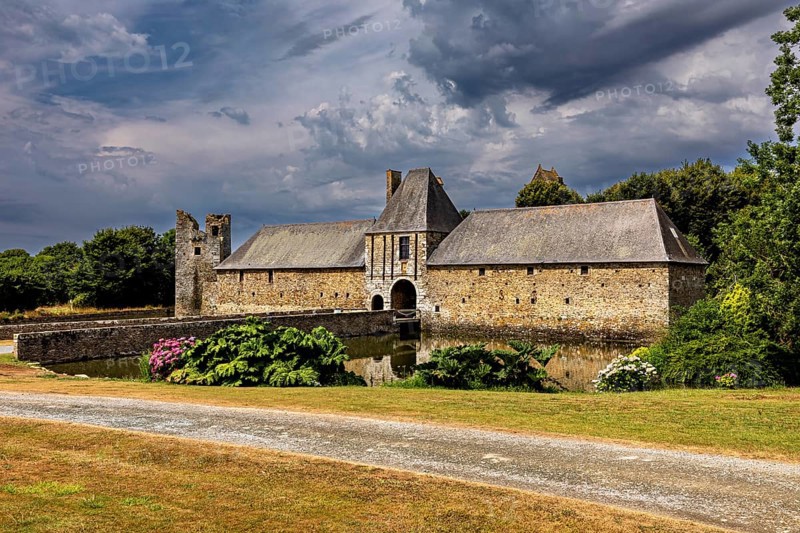 Historic castle with moat and garden under a dramatic sky, Gratot Castle in Normandy, France