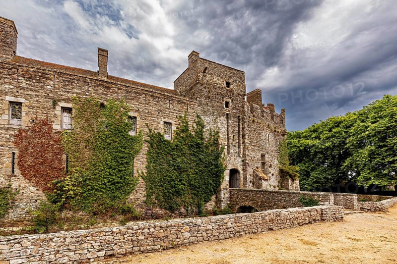 Side view of an old castle with ivy, under a cloudy sky, Pirou Castle in Normandy, France