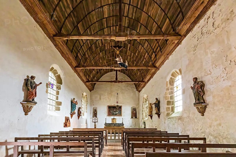 Interior view of a chapel with wooden ceiling, benches and statues on the walls, Pirou Castle in Normandy, France