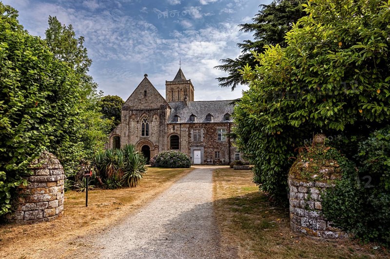 Historic church with a path surrounded by green trees and blooming nature, The Abbey de La Lucerne in Normandy, France