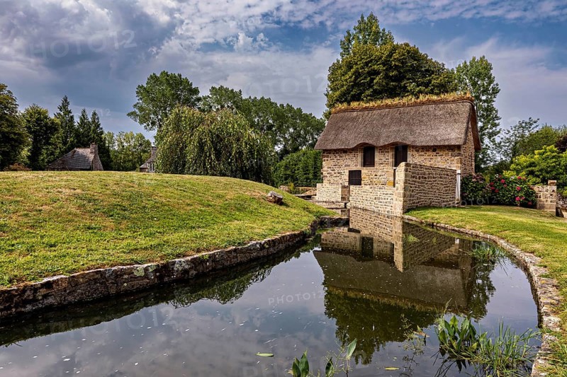 Small house with thatched roof in a quiet, green setting by a stream, The Abbey of La Lucerne in Normandy, France