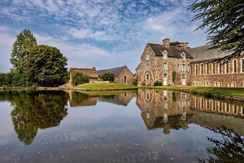 Historic castle on the shore of a lake with a clear reflection and surrounded by trees, The Abbey de La Lucerne in Normandy, France
