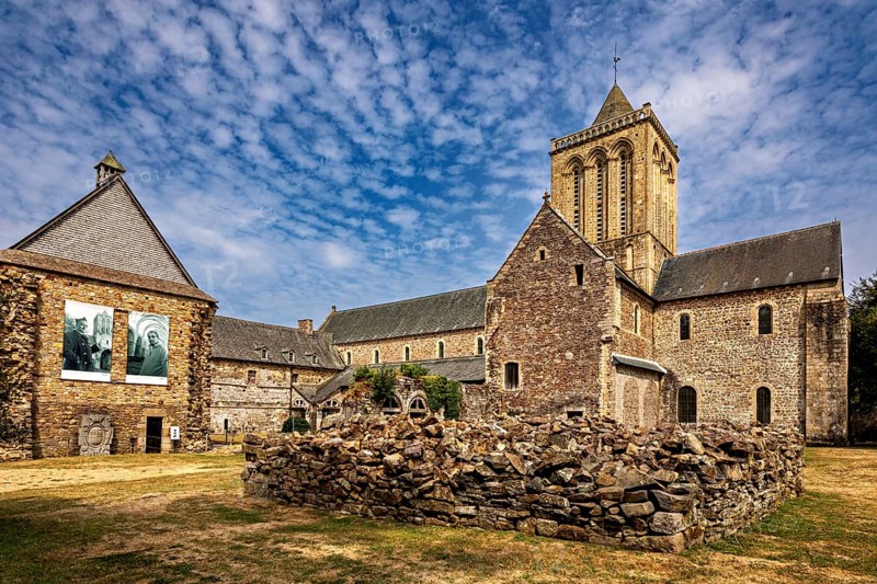 A church with adjoining ruins and stone walls under a blue sky, The Abbey de La Lucerne in Normandy, France