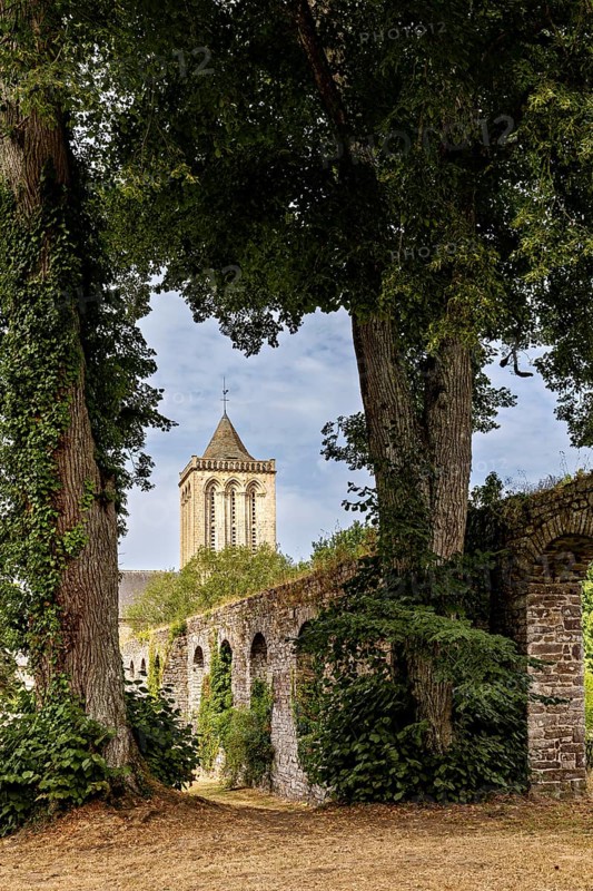 A tower surrounded by tall trees and an overgrown stone wall in a tranquil setting, The Abbey of La Lucerne in Normandy, France