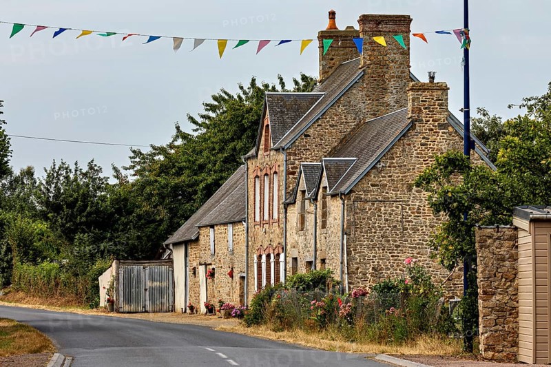 A traditional stone house on a rural road with festive garlands, Historic houses in Normandy, France