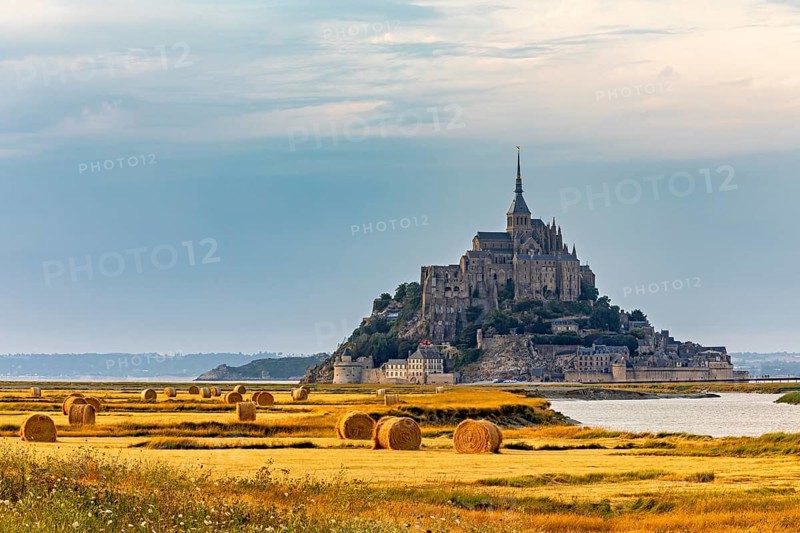 A historic castle under a cloudy evening sky surrounded by fields, Mont Saint Michel in Normandy, France