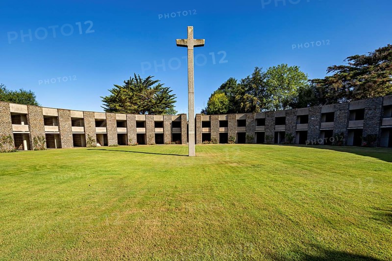 A stone cross sits enthroned in the centre of a green, circular courtyard surrounded by a concrete structure, German soldiers' cemetery from the Second World War near Huisnes-sur-Mer in Normandy, France