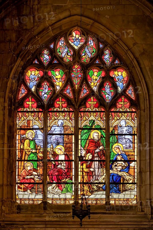 A Gothic stained glass window shows a religious scene with the Holy Family and angels in bright colours, The stained glass windows of Dieppe Cathedral in Normandy, France