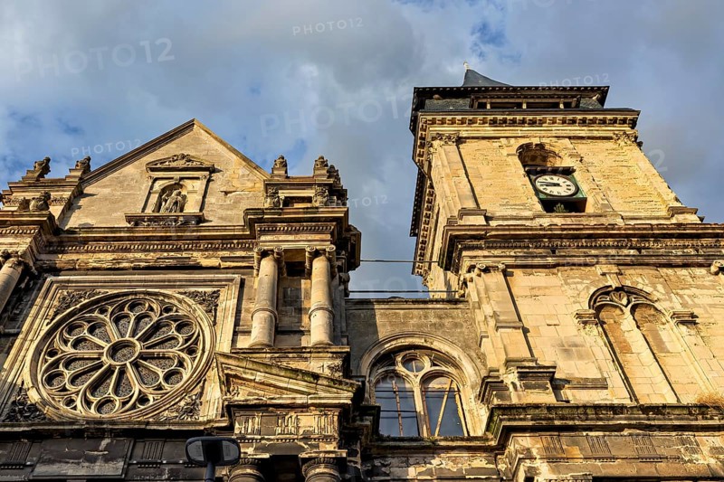 Detailed sandstone church façade with a clock and sculptures under a cloudy sky, Dieppe Cathedral in Normandy, France