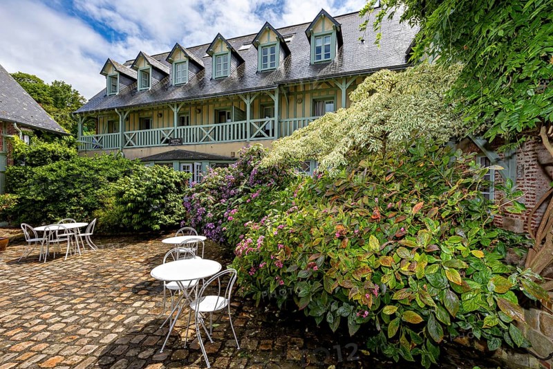 Lively garden with flowers and seating areas, surrounded by a backdrop of half-timbered houses, the historic mill village of Veules Les Roses in Normandy, France