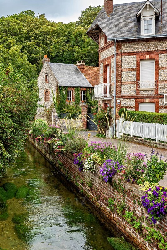 Beautifully landscaped canal with brick houses and flowers, surrounded by natural greenery, The historic mill village of Veules Les Roses in Normandy, France