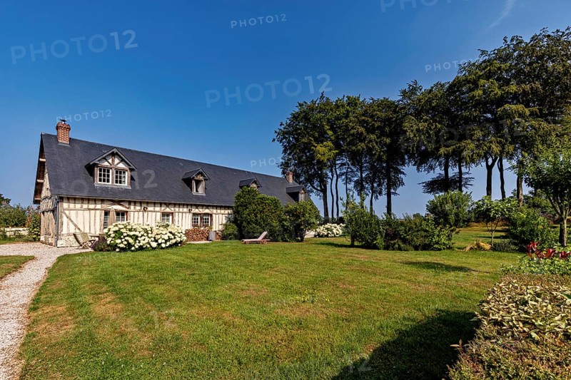 Inviting half-timbered house on a sunny day with a well-tended garden and stately trees, Historic houses in Normandy, France