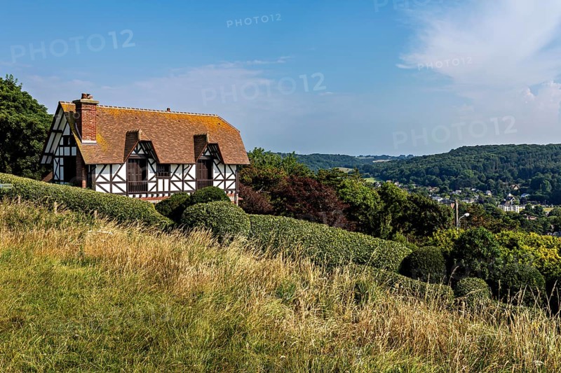 A half-timbered house on a hill surrounded by meadows and forests under a blue sky, Historic half-timbered house near Etretat in Normandy, France