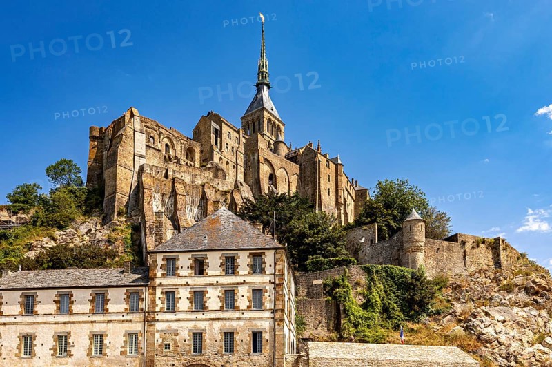 Imposing castle and fortress rising against a blue sky, with massive stone walls and towers, Mont Saint Michel in Normandy, France