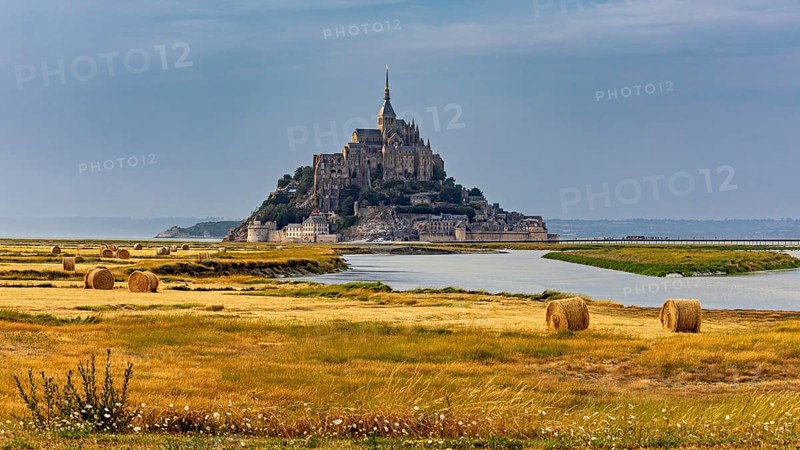 A castle rises in the middle of fields and a river, surrounded by bales of straw, Mont Saint Michel in Normandy, France
