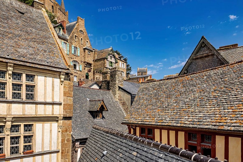 Varied roofs and half-timbered architecture in the foreground, with a historic castle in the background, Mont Saint Michel in Normandy, France