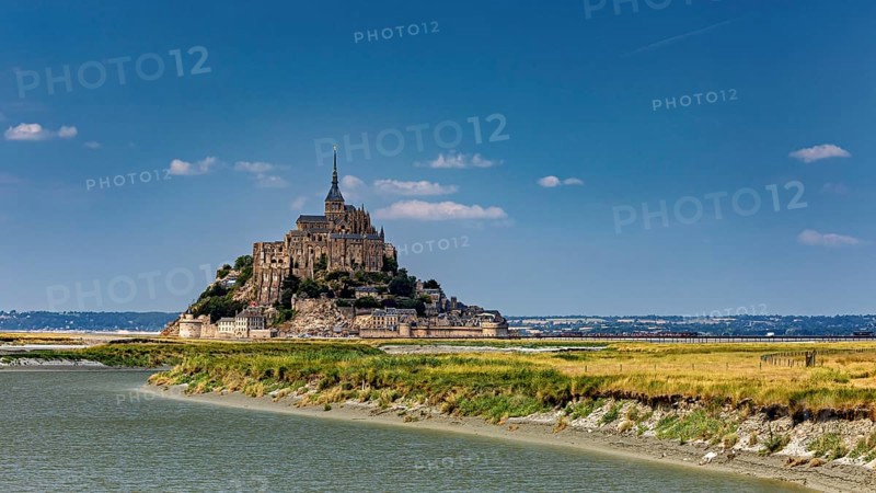 A majestic castle perched on the riverbank under a sunny sky, Mont Saint Michel in Normandy, France