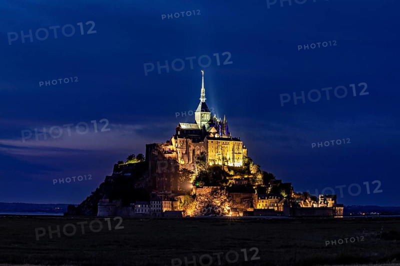 Historic monastery illuminated at night against a dark blue sky, Mont Saint Michel in Normandy, France