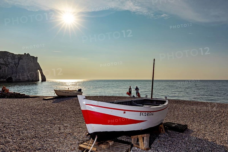 Tranquil beach scene at sunset with boat and people near cliffs, rowing boat at sunset on the coast of Etretat in Normandy, France
