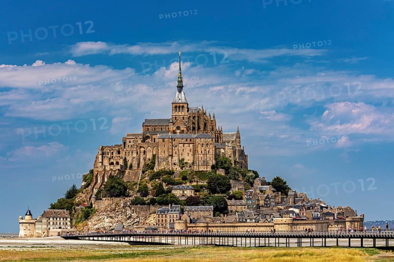 An imposing castle rises against a blue sky with a few clouds, Mont Saint Michel in Normandy, France