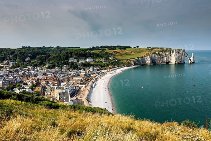 Coastal town with a bay surrounded by green hills, a lively beach promenade and clear water, The cliffs and alabaster coast of Etretat in Normandy France