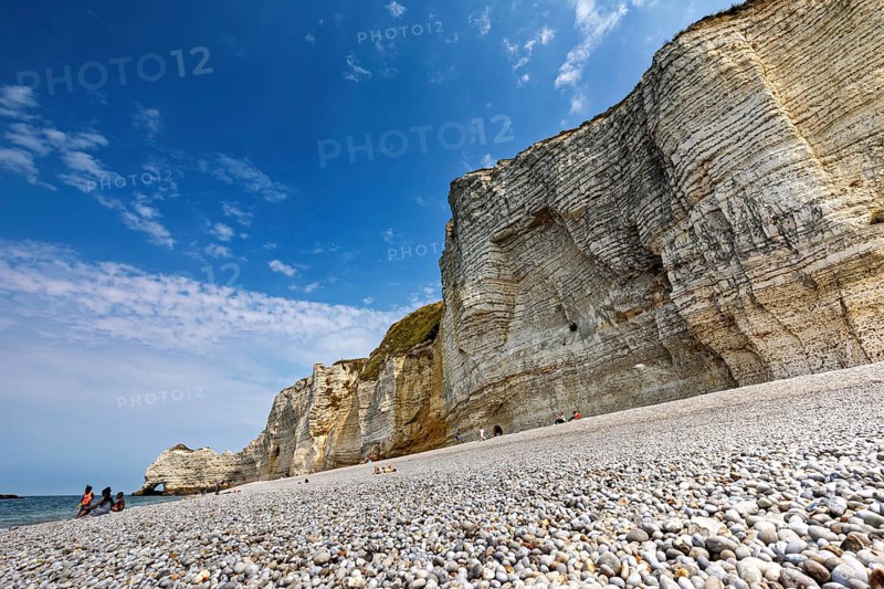 Pebble beach in front of high cliffs with blue sky and sea, The cliffs and alabaster coast of Etretat in Normandy France