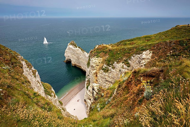 Green cliffs with sailing boat in the sea and small beach bay, The cliffs and alabaster coast of Etretat in Normandy France
