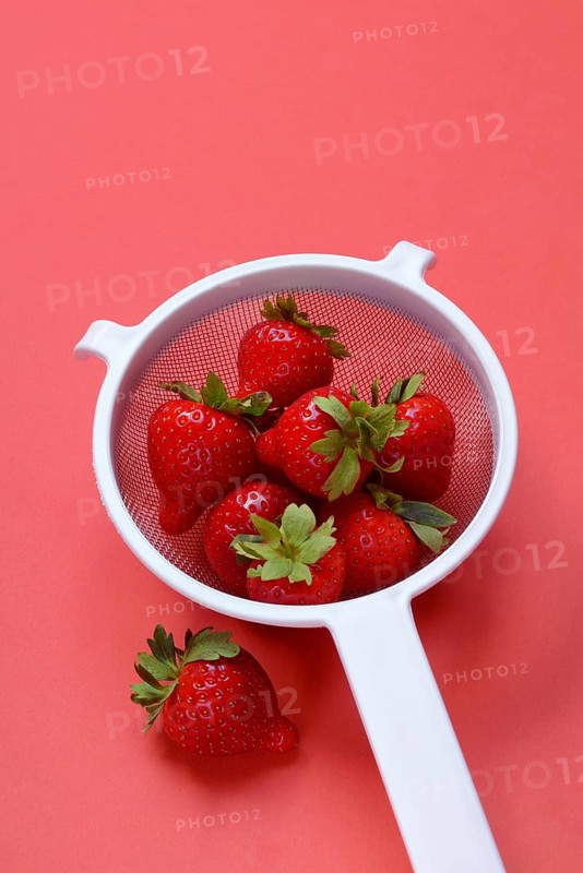 Strawberries in a colander on a red background, Fragaria