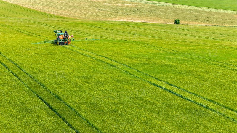 Farmer with tractor working in the field. In early summer, he fertilises the grain for an optimum yield. Drone photo. Merklingen, Baden-Württemberg, Germany