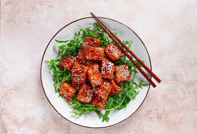Fried salmon slices, teriyaki with sesame seeds, with arugula salad, top view