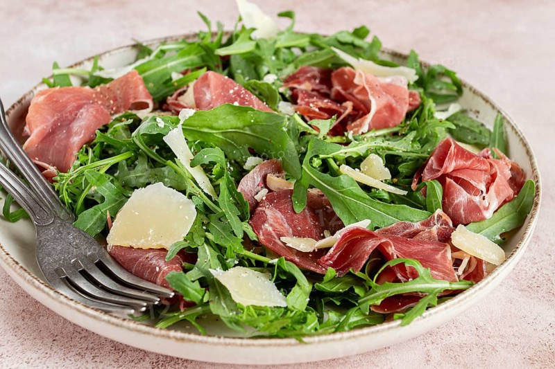 Fresh arugula salad with prosciutto and grated parmesan cheese, on a plate, homemade, no people