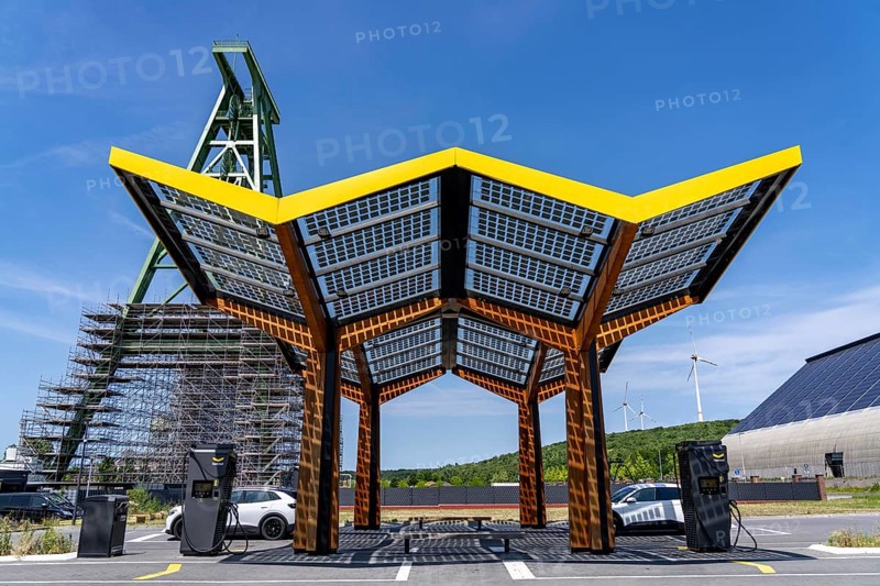 Electric filling station on the site of the former Lohberg colliery in Dinslaken, operated by Fastned, uses electricity from wind power and solar energy, fast-charging columns, with its own solar roof, in the background the 11, 500 square metre solar roof on the colliery's former coal mixing hall, wind farm on the Lohberg slagheap, Lohberg colliery headframe, North Rhine-Westphalia, Germany