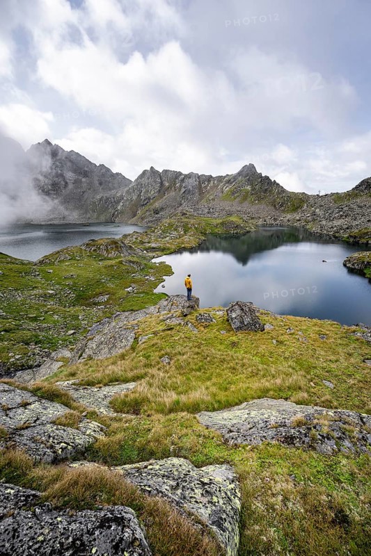 Mountaineer on a rock in front of mountain lakes Wangenitzsee and Kreuzsee, cloudy mountain peaks in the morning, Schober group, Hohe Tauern National Park, Carinthia, Austria