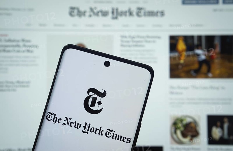 Dhaka, Bangladesh - 18 March 2025: The logo of the the new york times is displayed on a smartphone screen, and the website the new york times is visible on a computer screen in the background