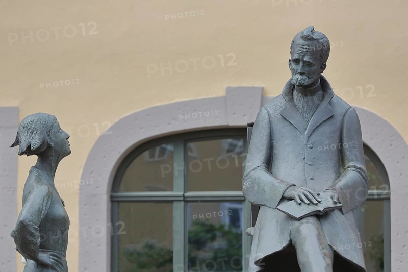 Monument to philosopher Friedrich Nietzsche, bronze sculpture, modern art, standing female figure, girl, sitting on chair, communication, conversation, listening, Holzmarkt, Saale, Naumburg, Saxony-Anhalt, Germany
