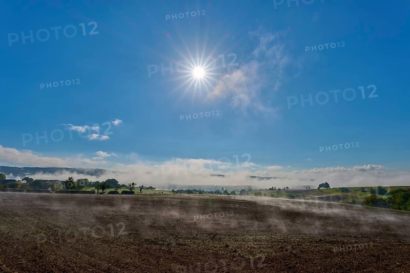 The sun shines brightly over a misty landscape stretching across wide fields, Mönchberg, Miltenberg, Spessart, Bavaria, Germany