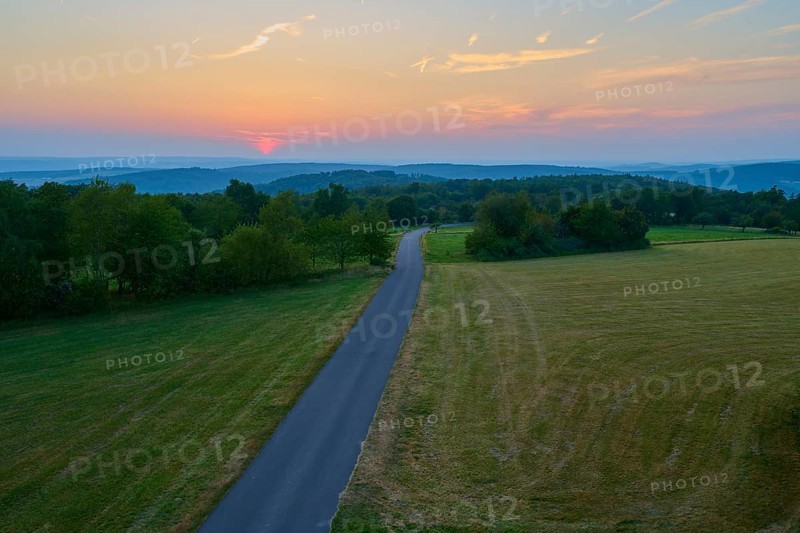Narrow road winds through fields at sunset with orange sky, Geishöhe, Dammbach, Spessart, Bavaria, Germany