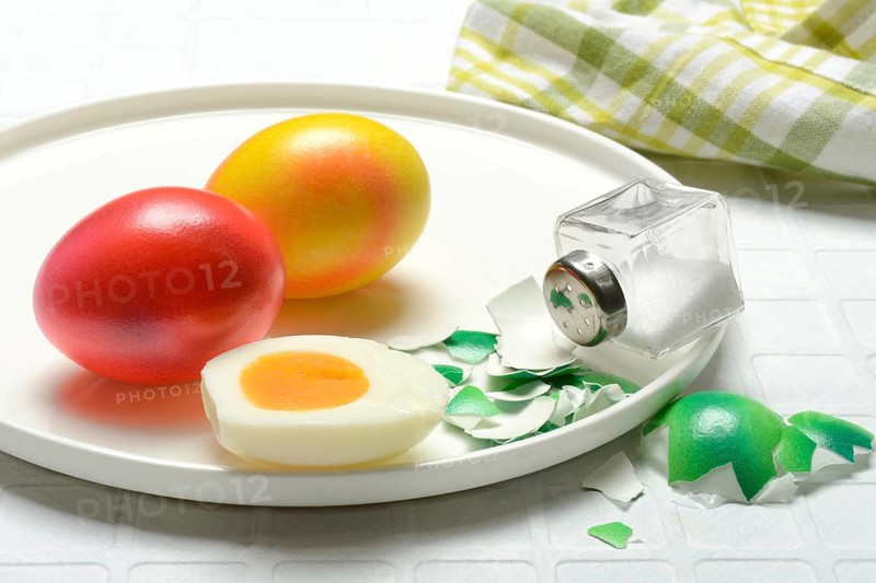Easter eggs and salt shaker on plate, partially peeled