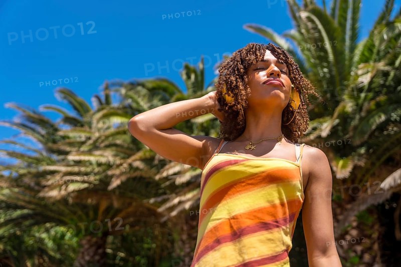 Young woman enjoying music with headphones in a tropical location, embracing the summer vibes and relaxing under palm trees