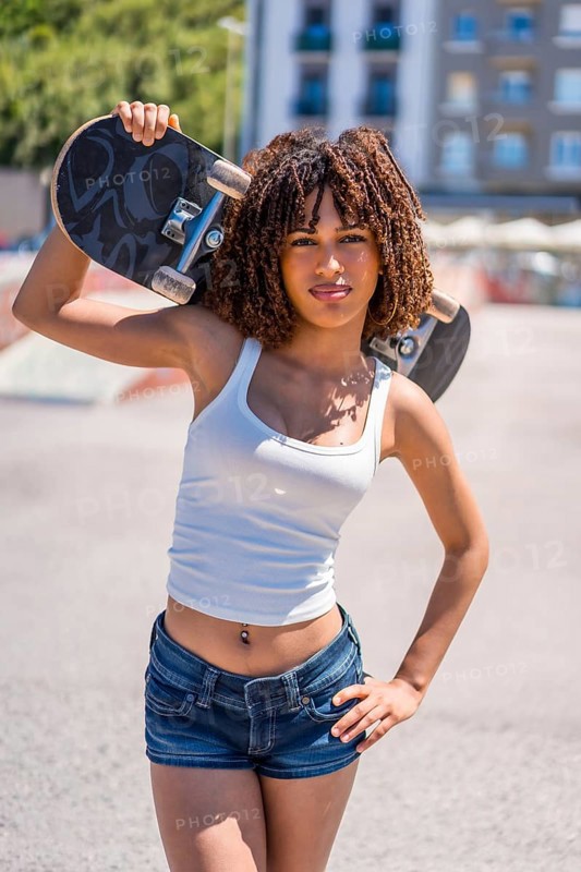 Stylish young woman holding her skateboard on her shoulder, showcasing a blend of confidence and urban cool