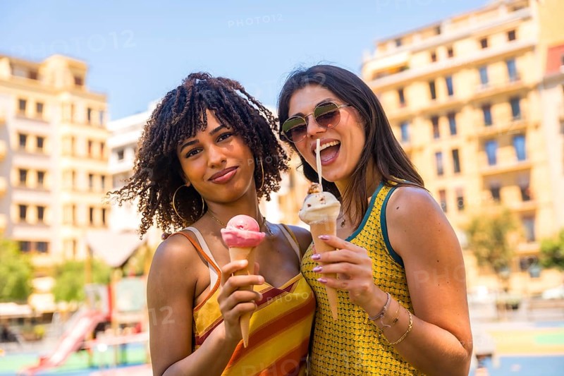 Two friends enjoying refreshing ice cream cones on a sunny day, sharing laughter and smiles in the vibrant city park atmosphere