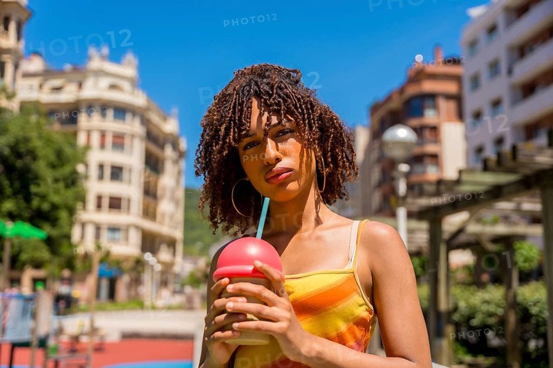 Fashionable young woman enjoys a cold beverage in a vibrant urban setting, embracing the summer vibes