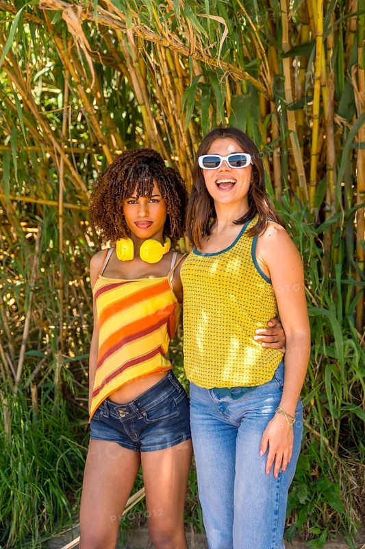 Two female friends hugging and smiling in a vibrant bamboo forest, soaking up the sun and enjoying their carefree day together