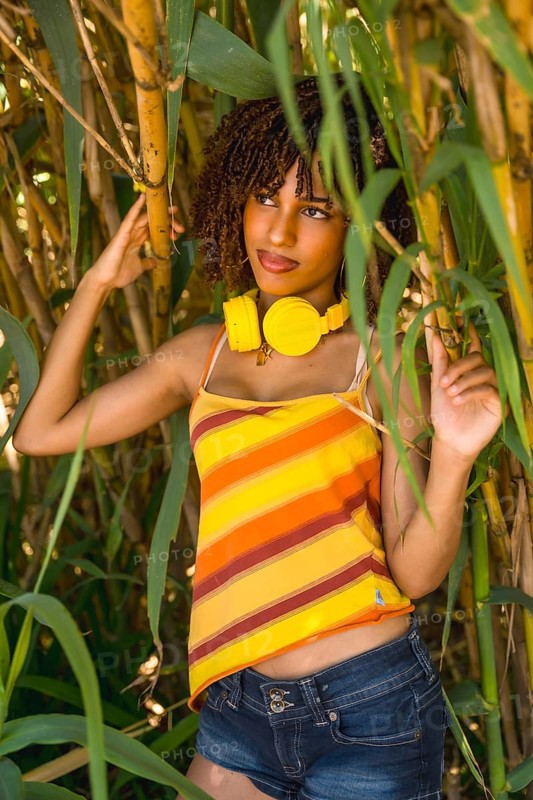Young woman with curly hair, wearing vibrant yellow headphones, immersing in music while surrounded by a serene bamboo forest