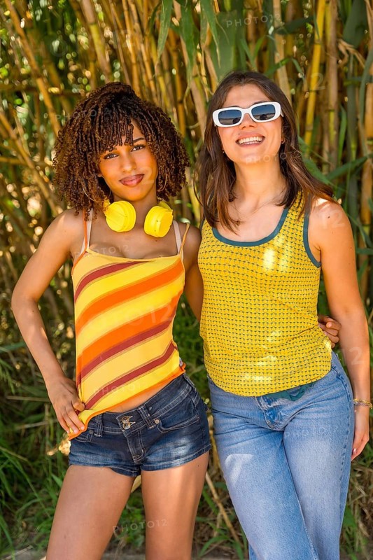 Two female friends posing together in a lush bamboo forest, soaking up the sun and embracing the joy of a vibrant summer day