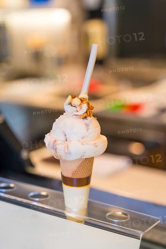 Delicious ice cream topped with nuts and chocolate, served in a waffle cone, sitting enticingly on a store counter, ready for enjoyment