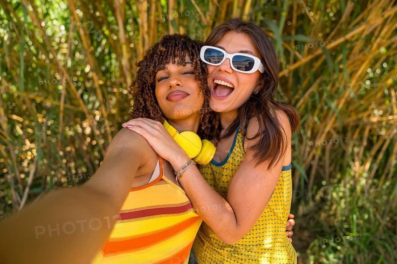 Two cheerful young women hug and take a selfie in a bamboo forest, enjoying their summer vacation together