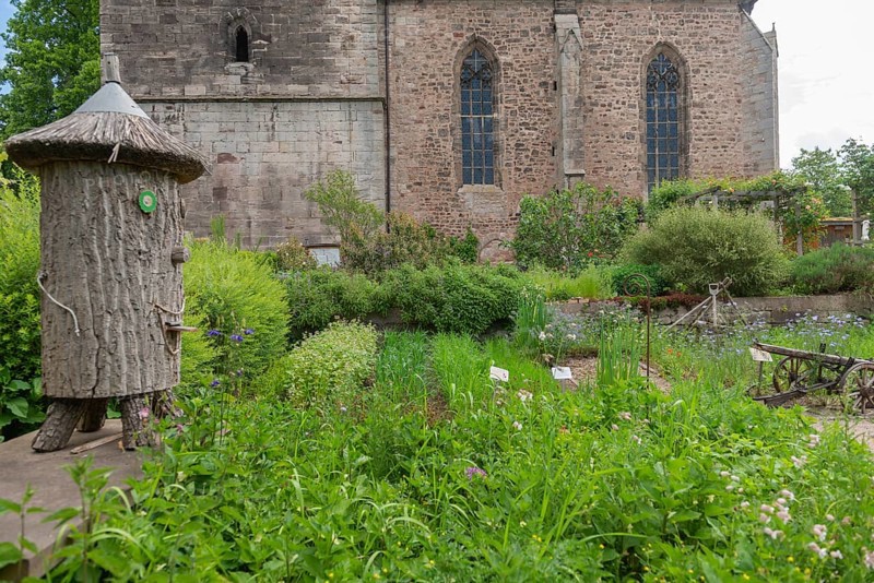 Church and Bible garden of St. Crucis Church, Bad Sooden, Allendorf, Allendorf district, symbol of paradise garden with biblical flora, beds, fruits of the field, agricultural implements, plough, beekeeping in a log hive, tree trunk, thatched roof, fieldstone church, Werra-Meissner district, Hesse, Germany