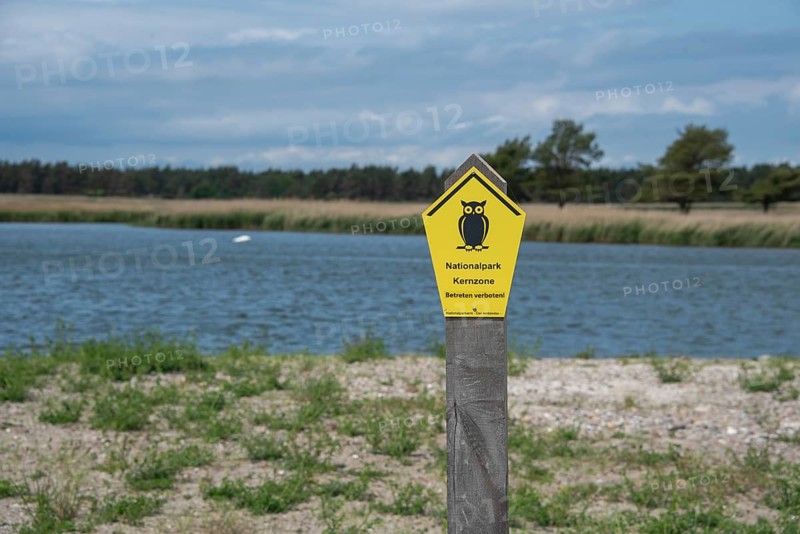 Yellow national park sign with owl in the foreground, water and cloudy sky in the background, Prerow, Mecklenburg-Vorpommern, Germany